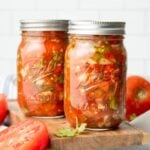Two mason jars filled with salsa sit on a wooden cutting board with tomatoes around them