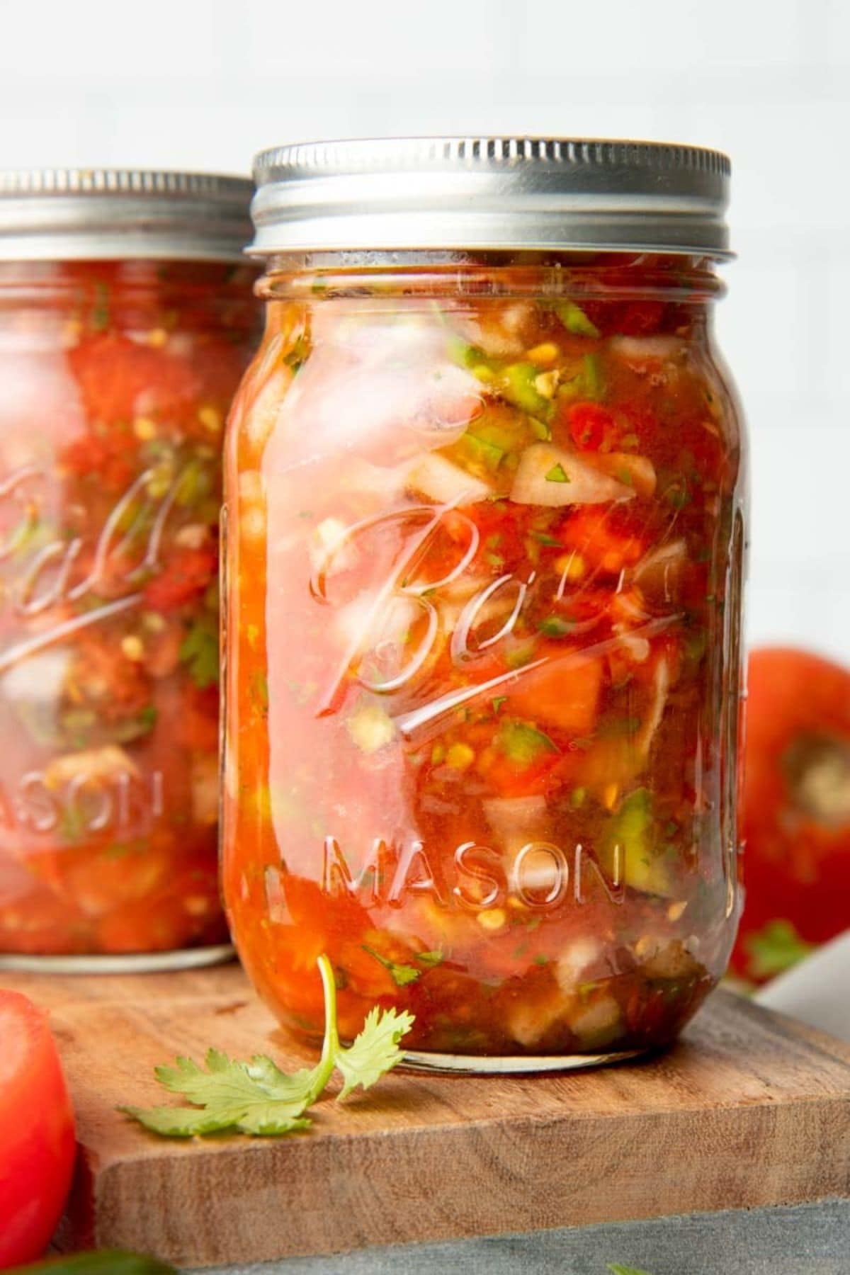 Two mason jars filled with salsa sit on a wooden cutting board