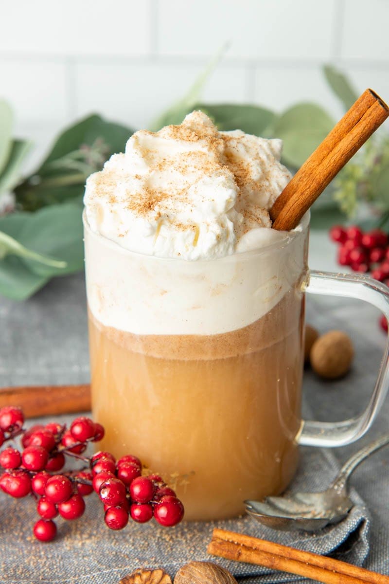 Close-up of a full mug of hot buttered rum with whipped cream, nutmeg, and cinnamon stick garnish.