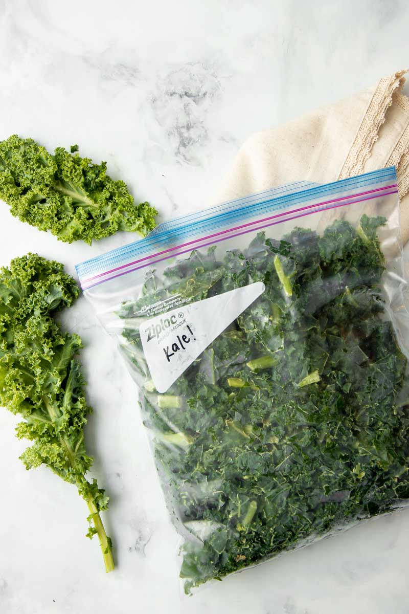 Frozen kale in a closed, zip-top bag with fresh kale beside it.