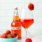 A glass of homemade strawberry wine sits next to a bowl of fresh strawberries.