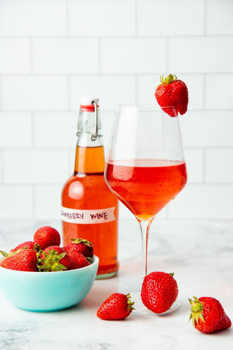 A glass of homemade strawberry wine sits next to a bowl of fresh strawberries.