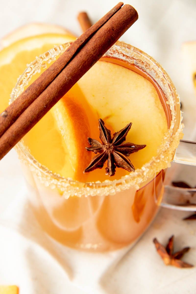 The top of a mug of spiked apple cider showing the sugar rim, cinnamon stick, and star anise garnishes close up.