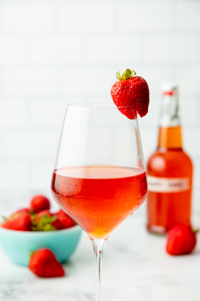 Close-up of a glass of chilled strawberry wine with a fresh strawberry garnish.