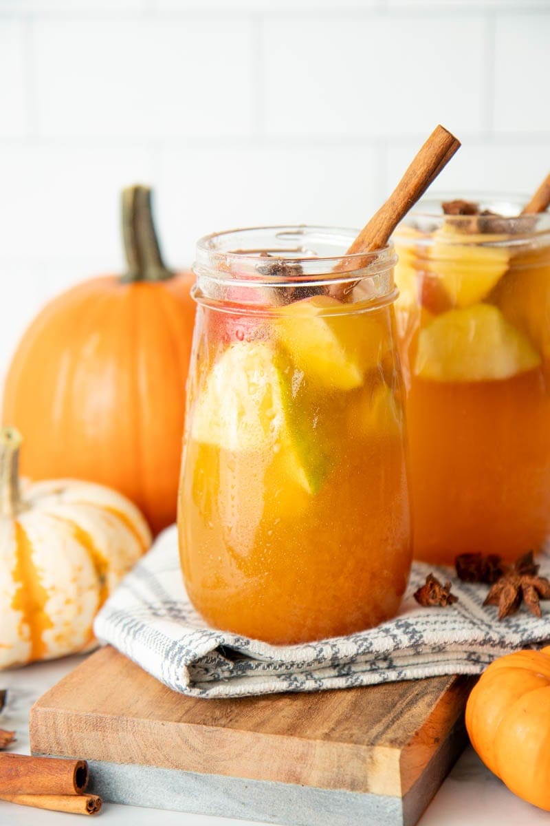 Two glasses of fall sangria sit on a kitchen linen surrounded by pumpkins and whole spices.