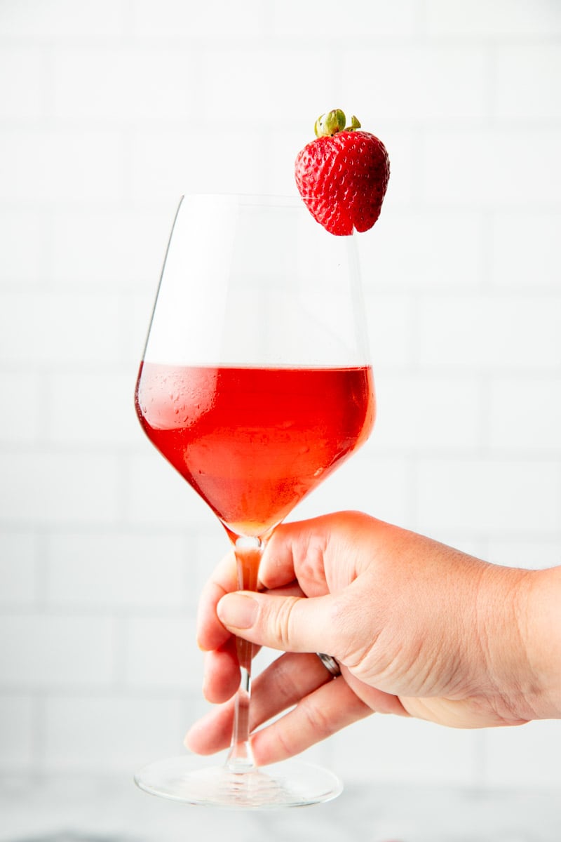 Close-up of hand holding a glass of strawberry wine.