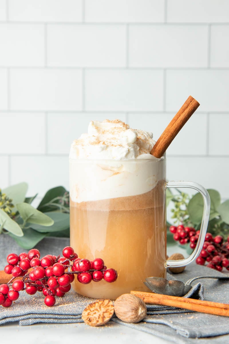 A glass mug filled with hot buttered rum, topped with whipped cream, and garnished with nutmeg and a cinnamon stick.
