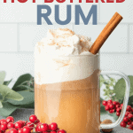 A glass mug filled with hot buttered rum, topped with whipped cream, and garnished with nutmeg and a cinnamon stick. A text overlay reads, "Single Drink or For a Crowd! Hot Buttered Rum."