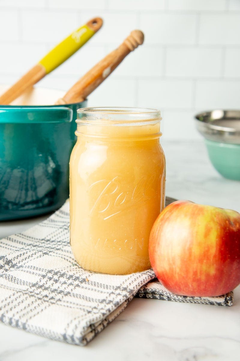 A full pint jar of applesauce for canning sits next to a fresh apple.