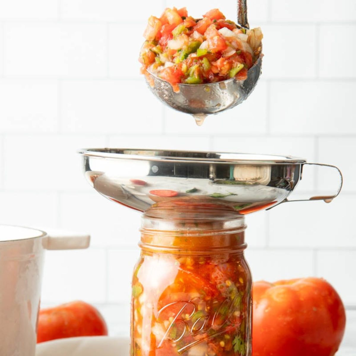 A ladle spoons salsa into a canning jar