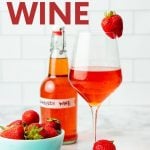 A glass of homemade strawberry wine sits next to a bowl of fresh strawberries. A text overlay reads, "How to Make Strawberry Wine."