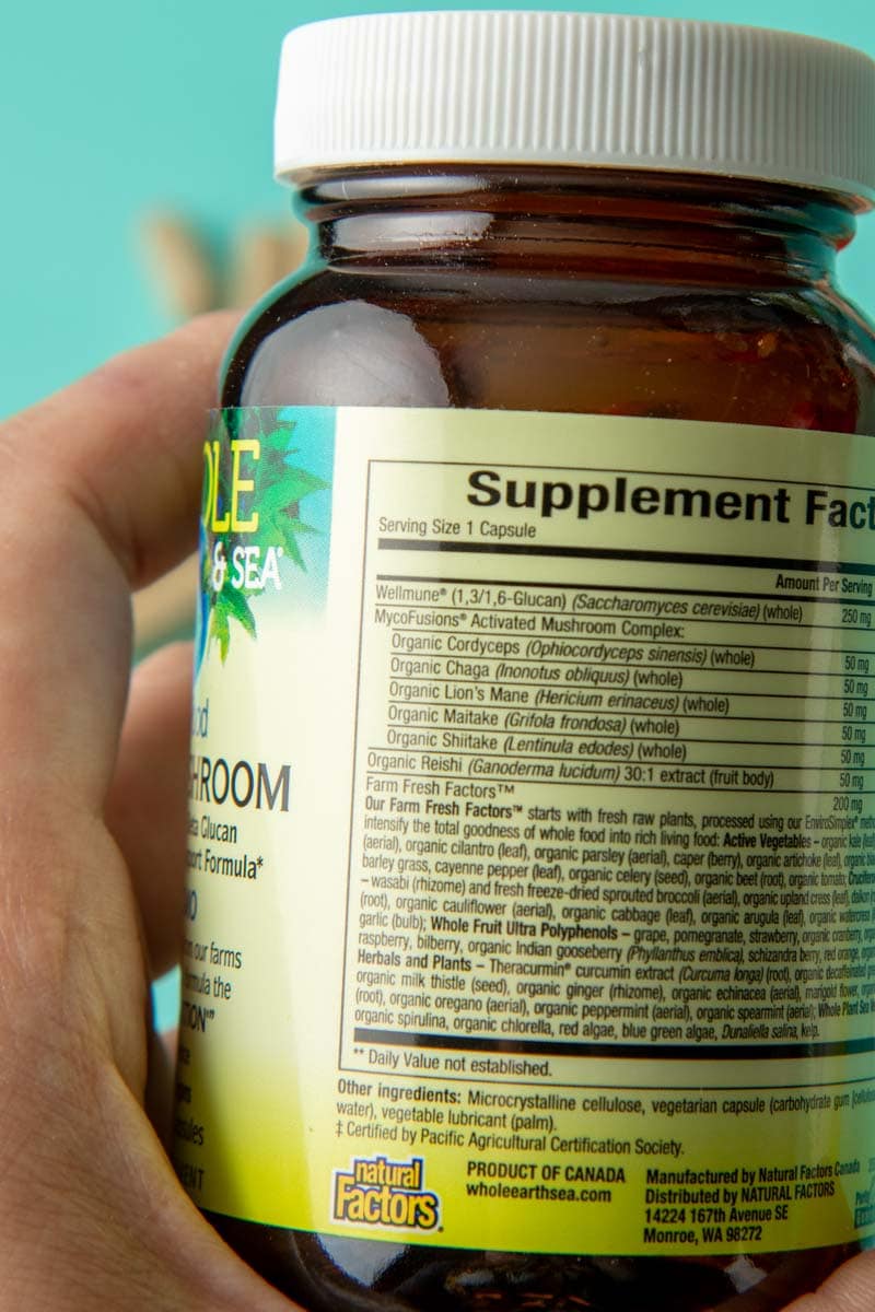 Close-up of a hand holding a bottle of herbal supplements to show the label on the back listing its organic ingredients.