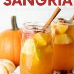 Two glasses of pumpkin sangria sit on a kitchen linen surrounded by pumpkins and whole spices. A text overlay reads, "Pumpkin Pie Sangria."