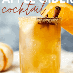 Chilled glass of spiked cider filled with with ice and garnished with sugar rim, cinnamon stick, star anise pod, and orange slice. A text overlay reads, "Bourbon Apple Cider Cocktail."