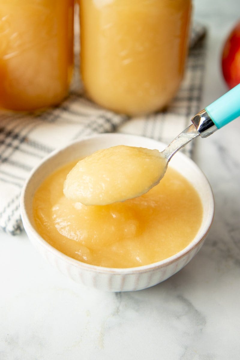 A full bowl of homemade applesauce with a spoonful above it.