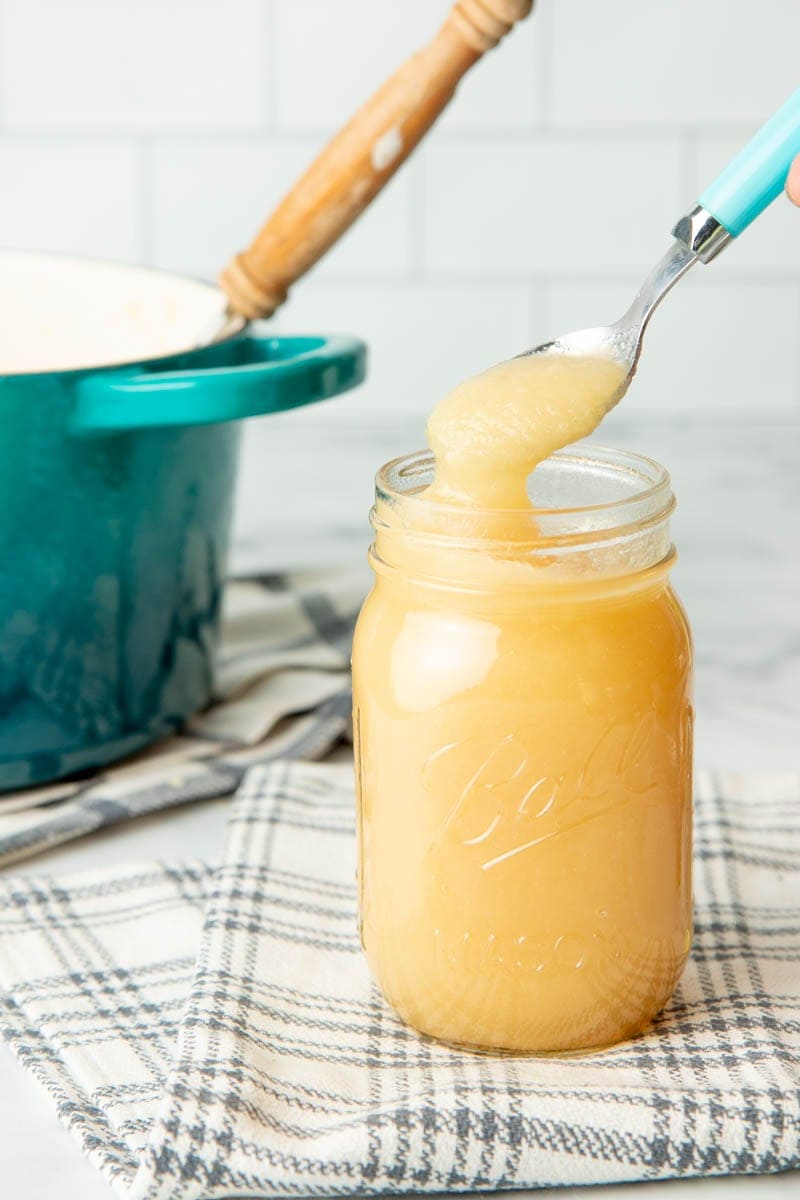 A spoon takes a spoonful of canned applesauce out of a full pint jar.