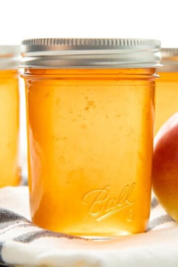 Three jars of golden apple jelly sit on a kitchen towel