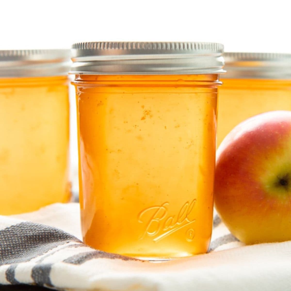 Three jars of golden apple jelly sit on a kitchen towel