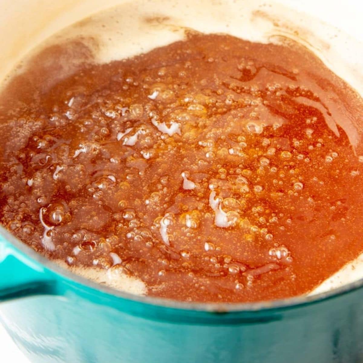 Apple jelly boiling in a teal Dutch oven