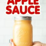 A hand holds a mason jar of applesauce with the text overlay "How to Can Applesauce"