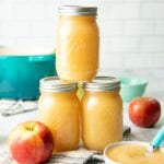 Three jars of canned applesauce stacked on a white countertop