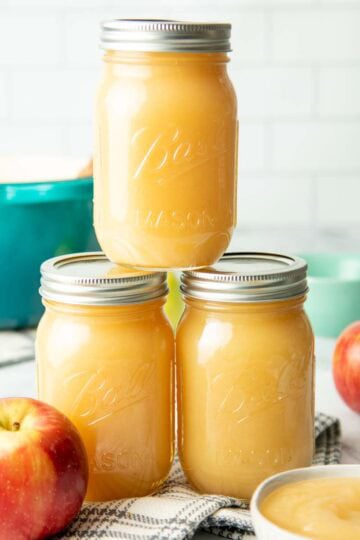 Three jars of canned applesauce stacked on a white countertop