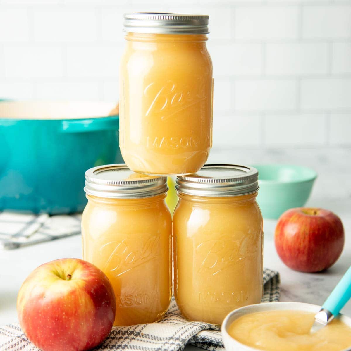 Three jars of canned applesauce stacked on a white countertop