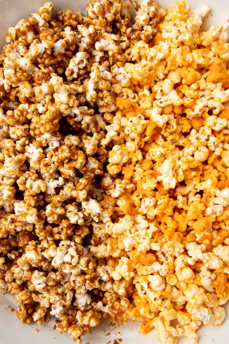 Homemade cheese and caramel popcorn side by side in a large mixing bowl.