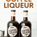 Two glass bottles of homemade Kahlua stand side-by-side surrounded by coffee beans. A text overlay reads, "Homemade Coffee Liqueur."
