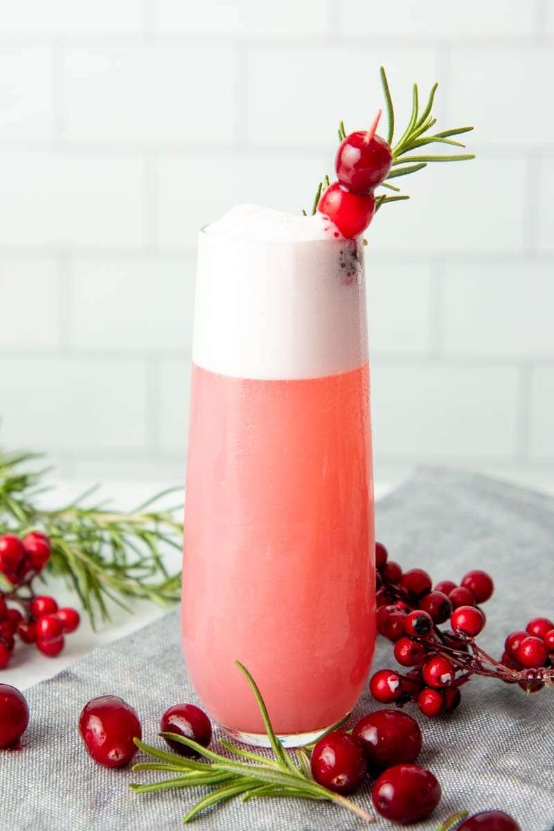 Close-up of a tall glass of cranberry gin fizz garnished with fresh cranberries and a rosemary sprig.