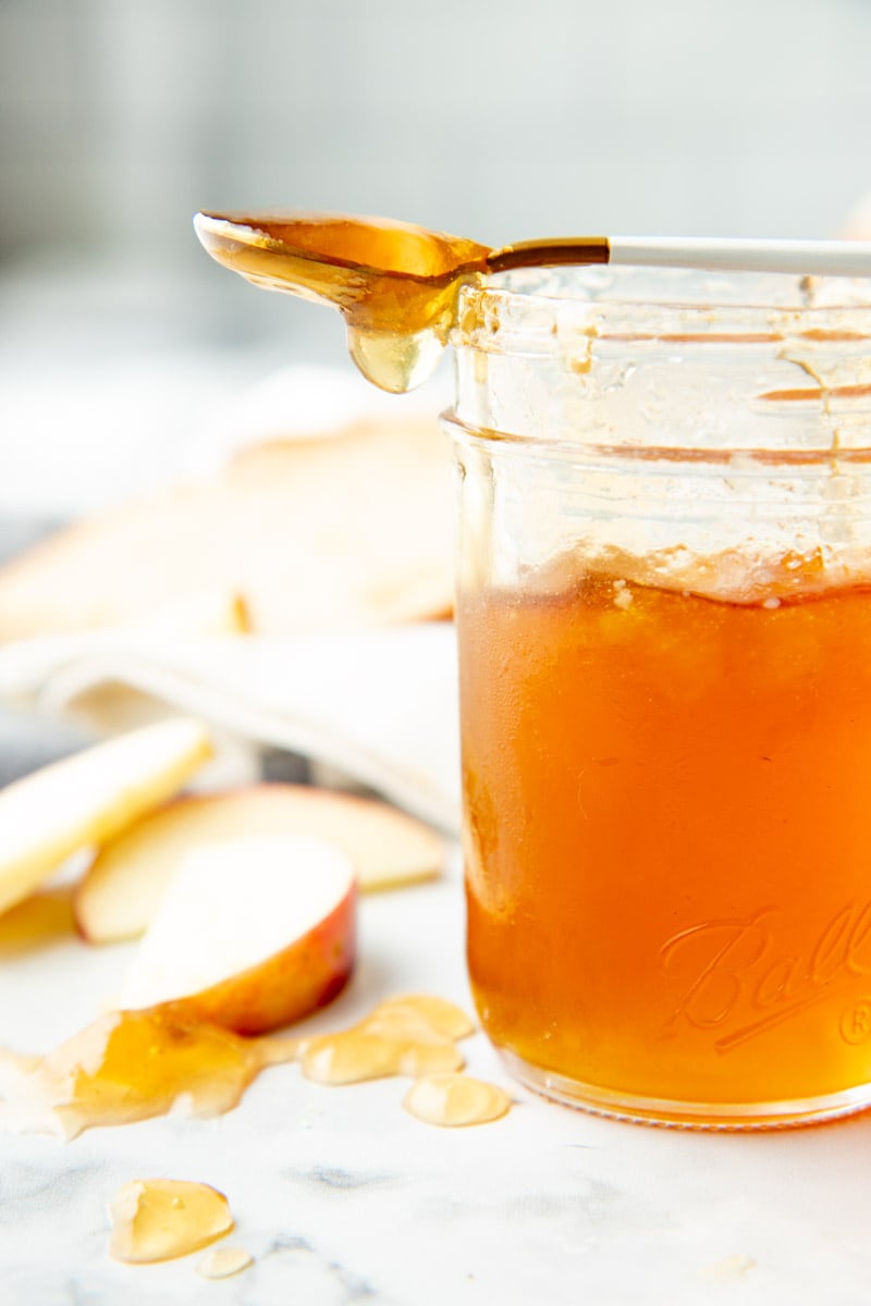 A spoon dripping apple jelly rests across the top of a jar of finished jelly.