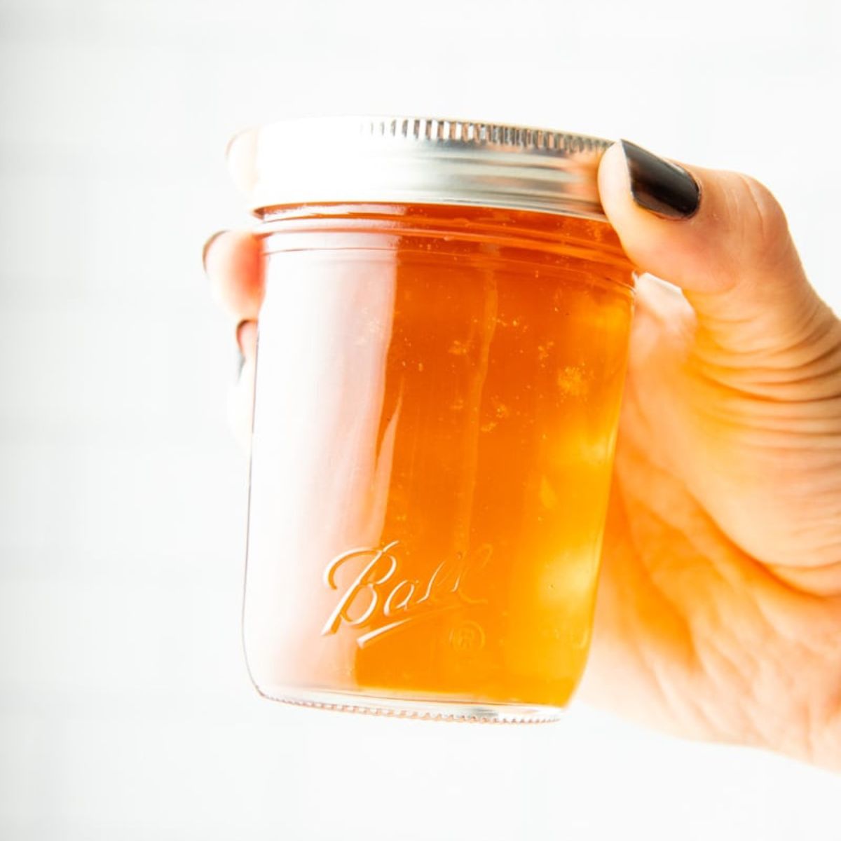 A hand holds a finished canning jar of golden apple jelly