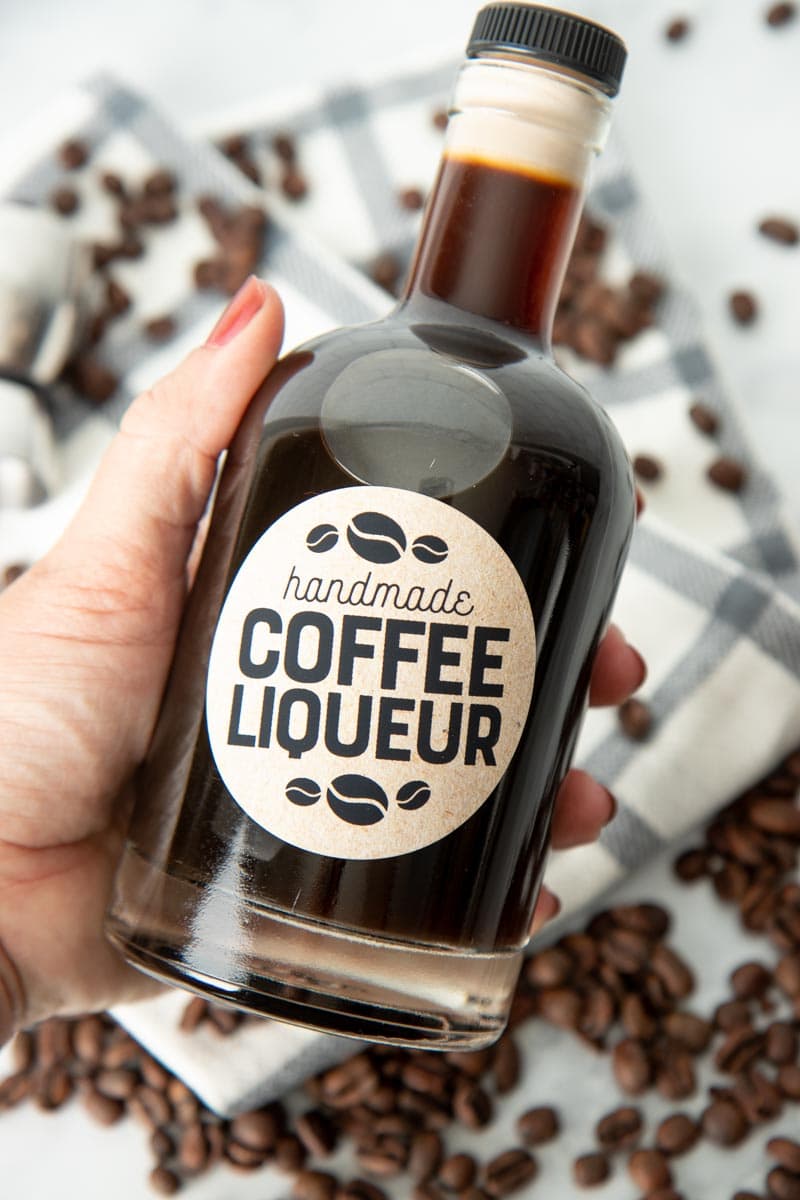 A hand holds a glass bottle filled with homemade coffee liqueur.