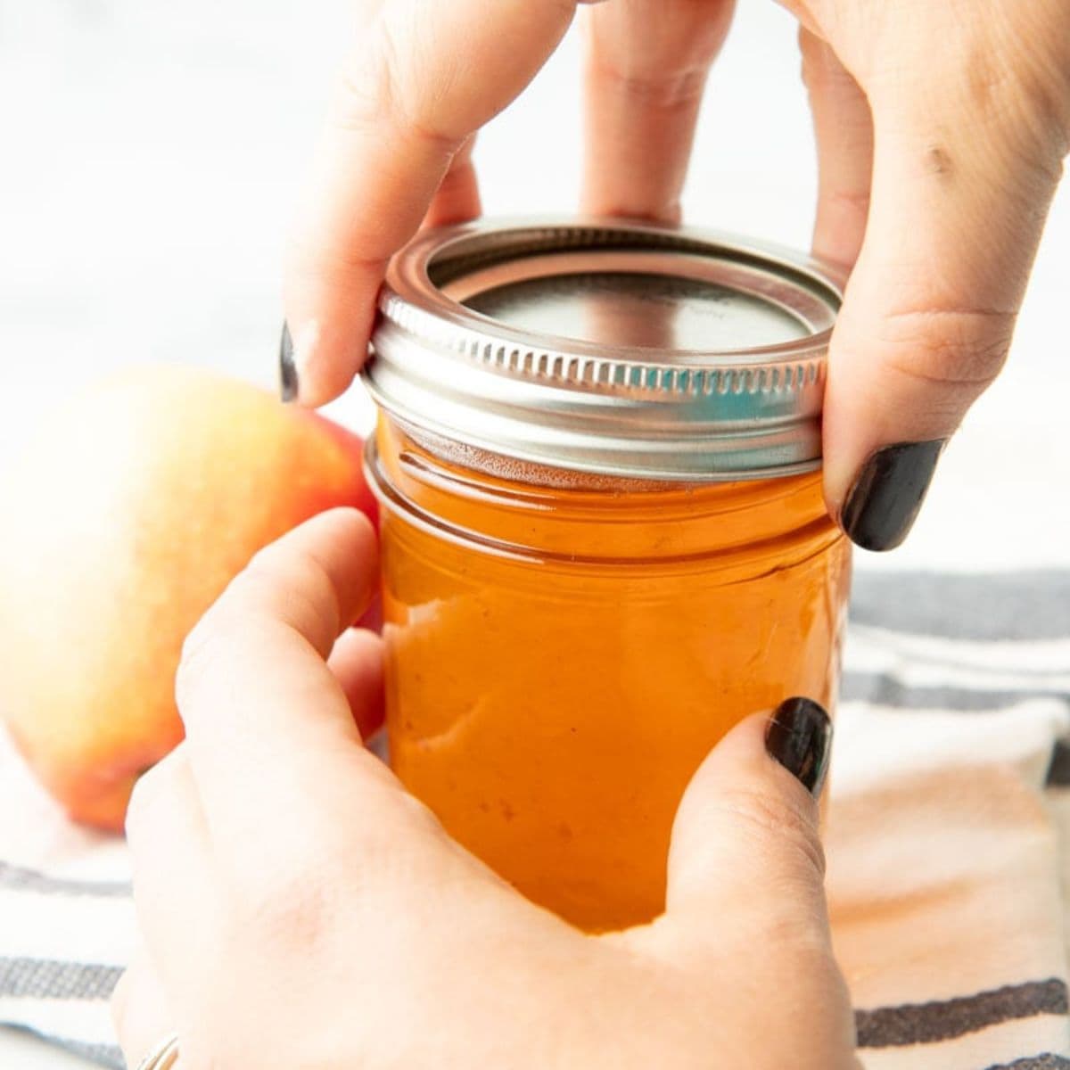 Screwing lid onto a canning jar filled with apple jelly