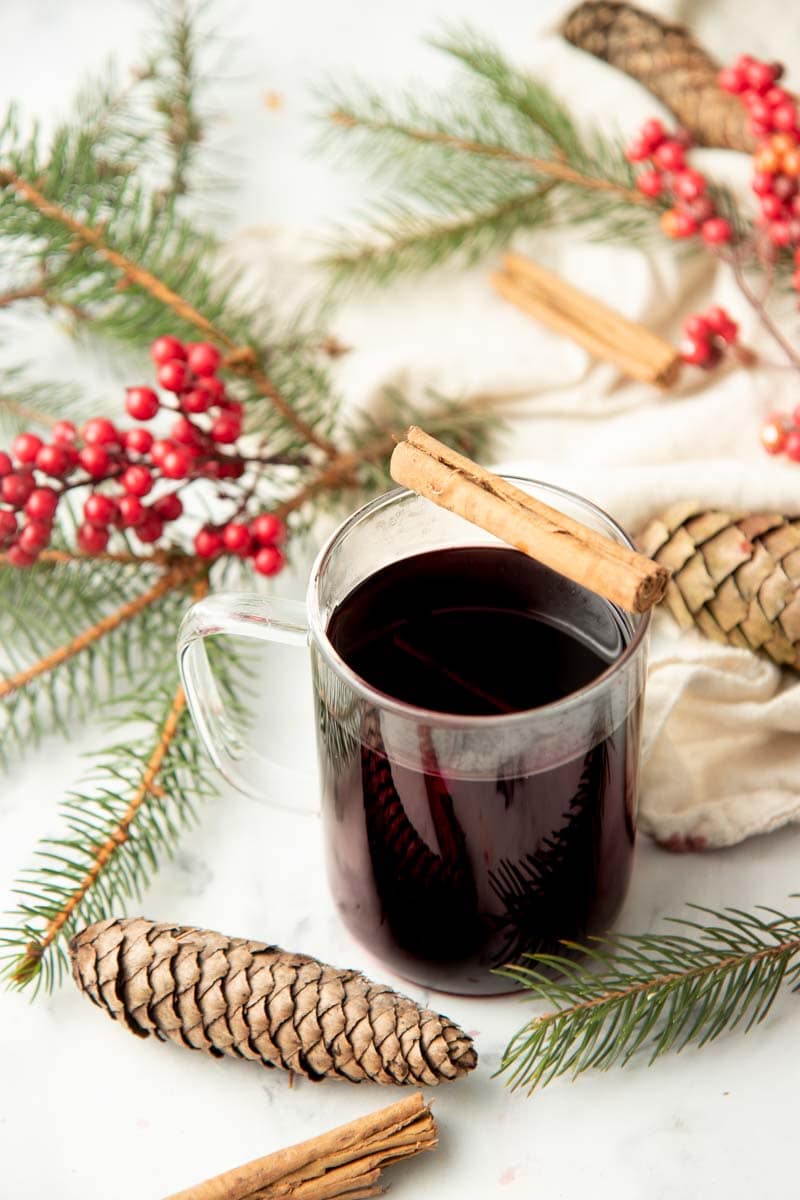 A mug of wassail sits surrounded by pine branches and pine cones.