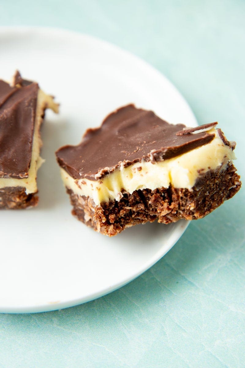Close-up of a nanaimo bar with a bite taken out of it on the edge of a plate.