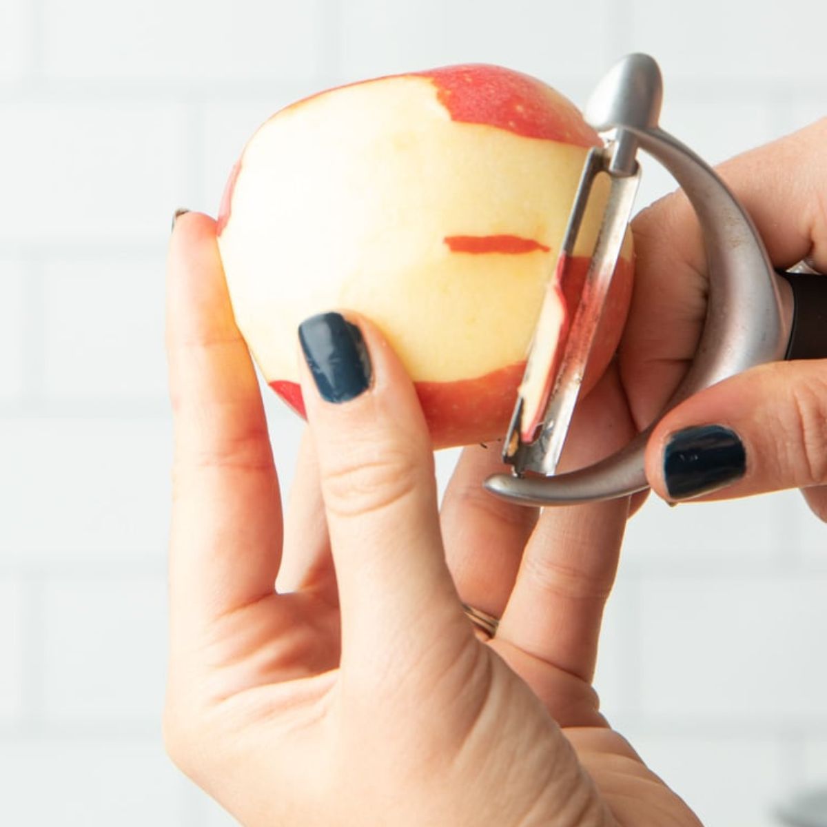 Hands peeling a red apple using a vegetable peeler