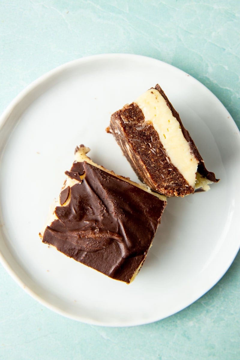 Overhead of two nanaimo bars on a plate with one on its side to show its layers.