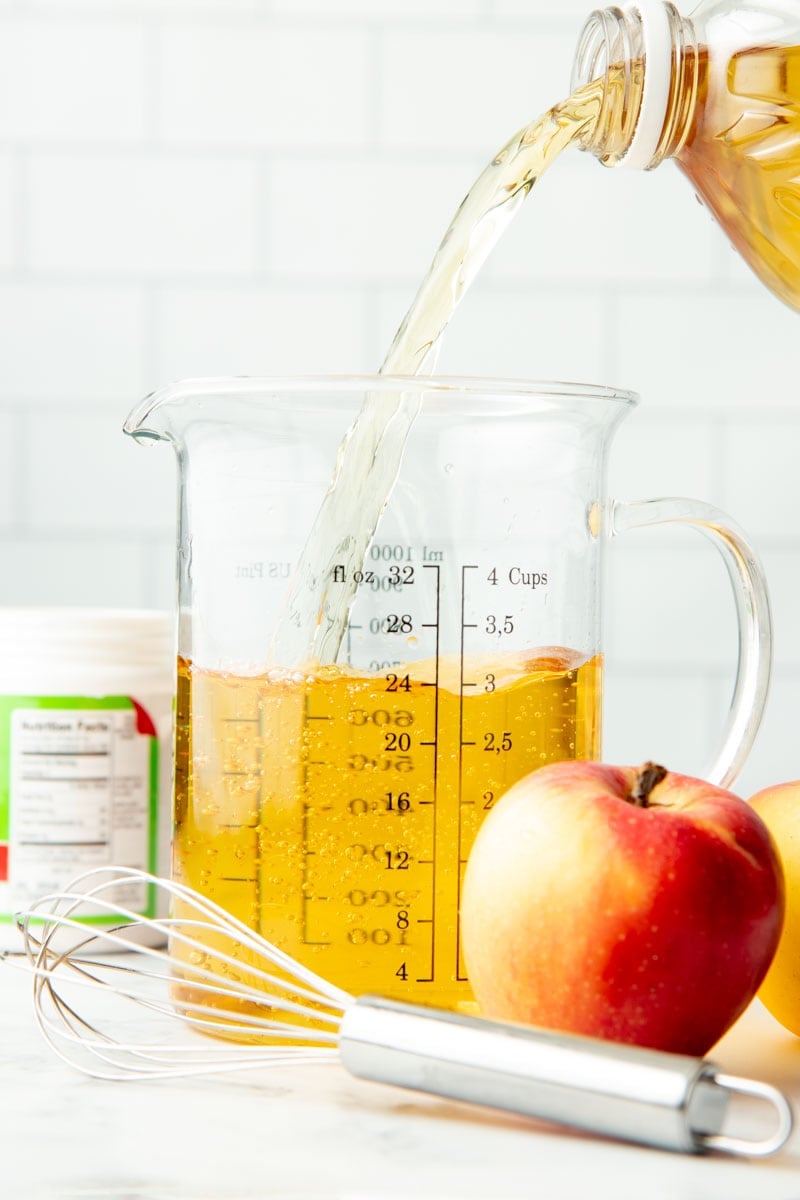 Pouring apple juice into a four-cup, glass measuring cup.