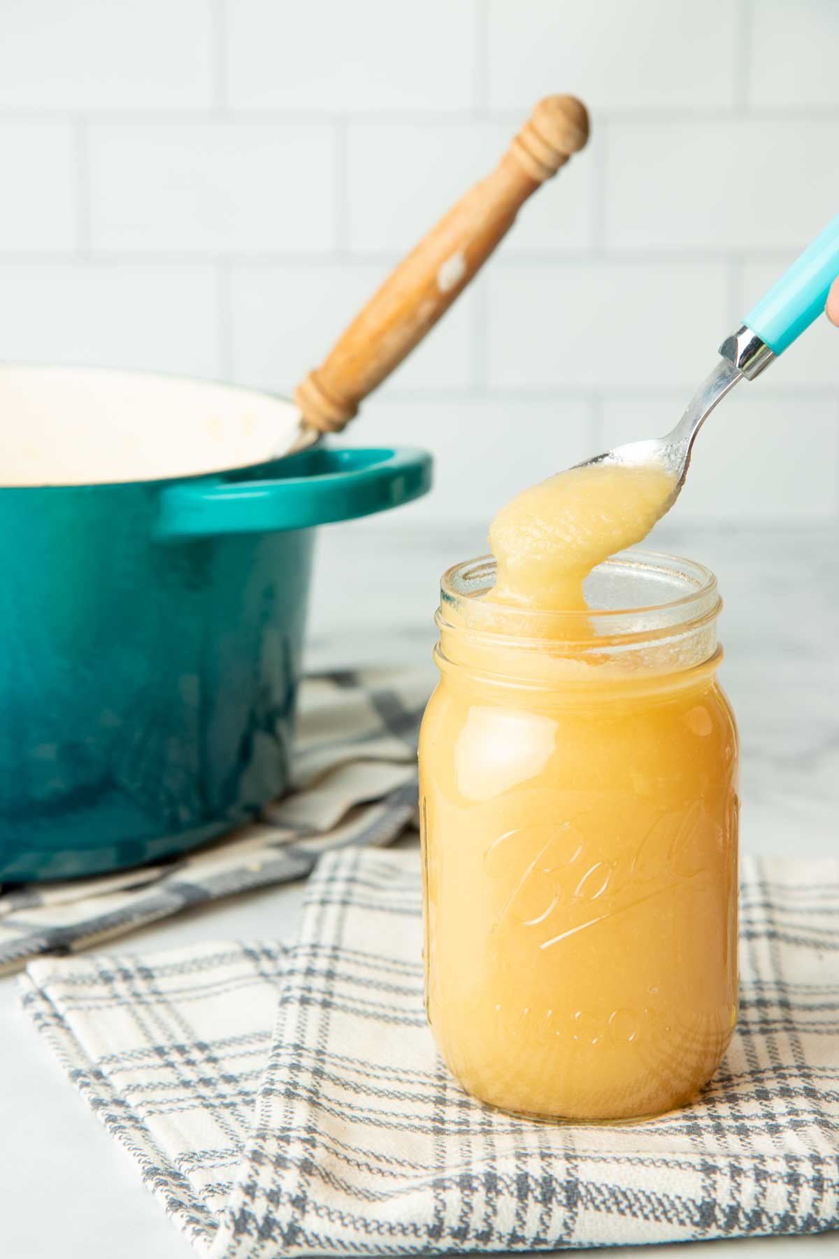 Spooning applesauce out of a canning jar with a teal Dutch oven in the background