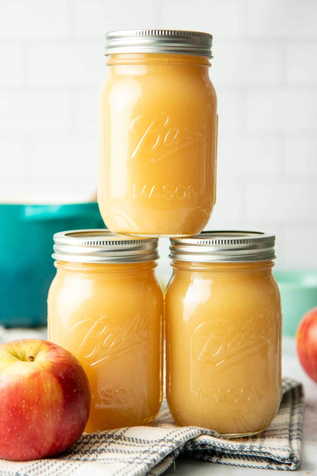 Three canning jars filled with applesauce stack in a white kitchen