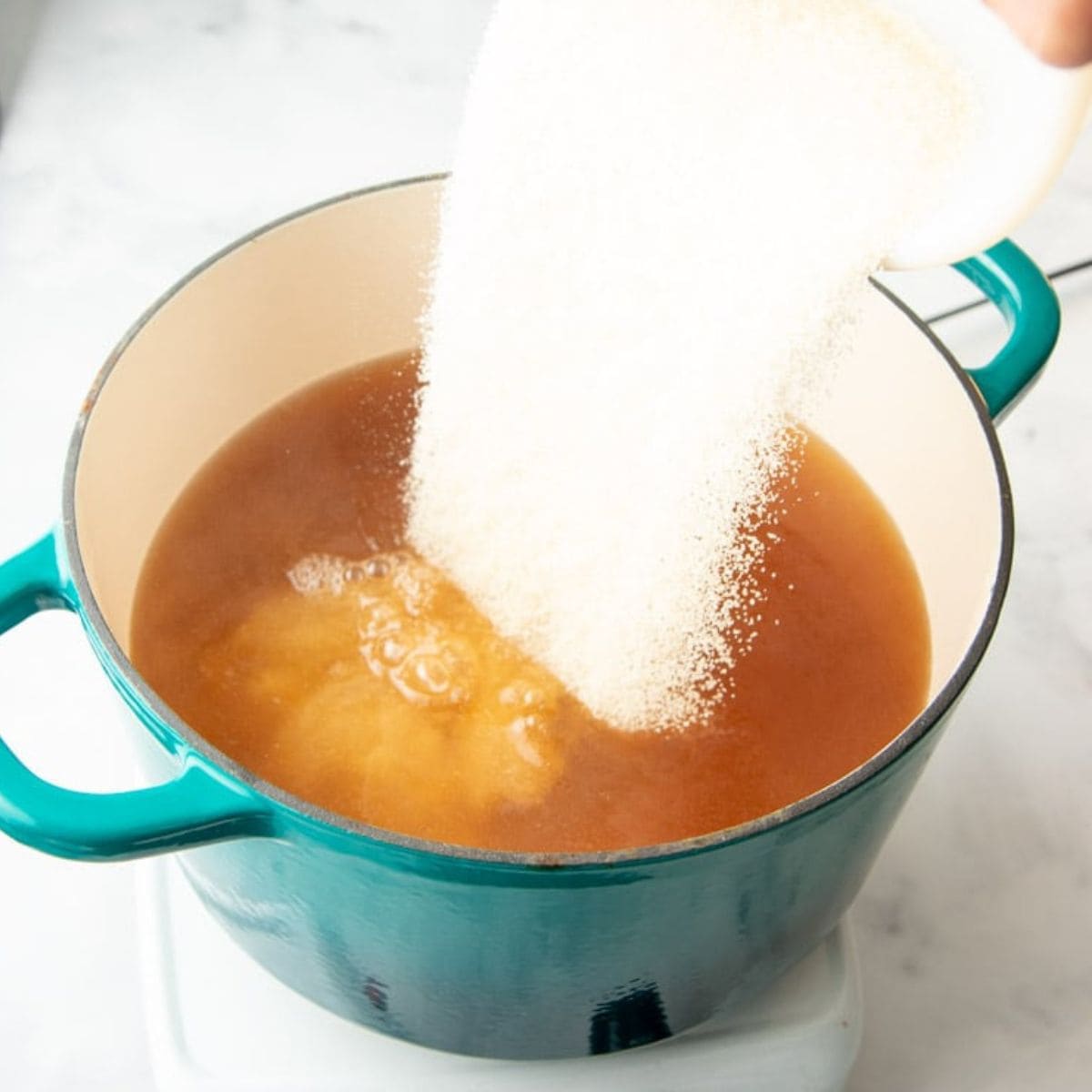 Pouring sugar into apple jelly in a Dutch oven