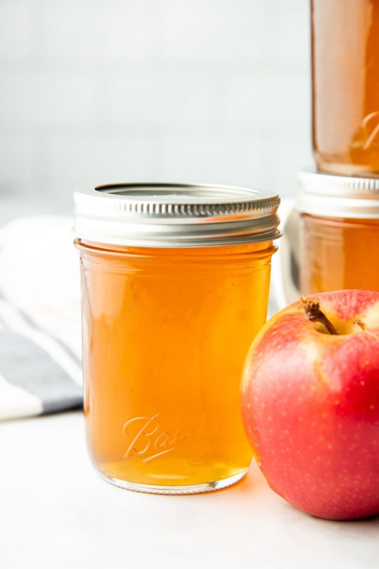 Close-up of a canned jar of apple jelly next to a fresh apple.