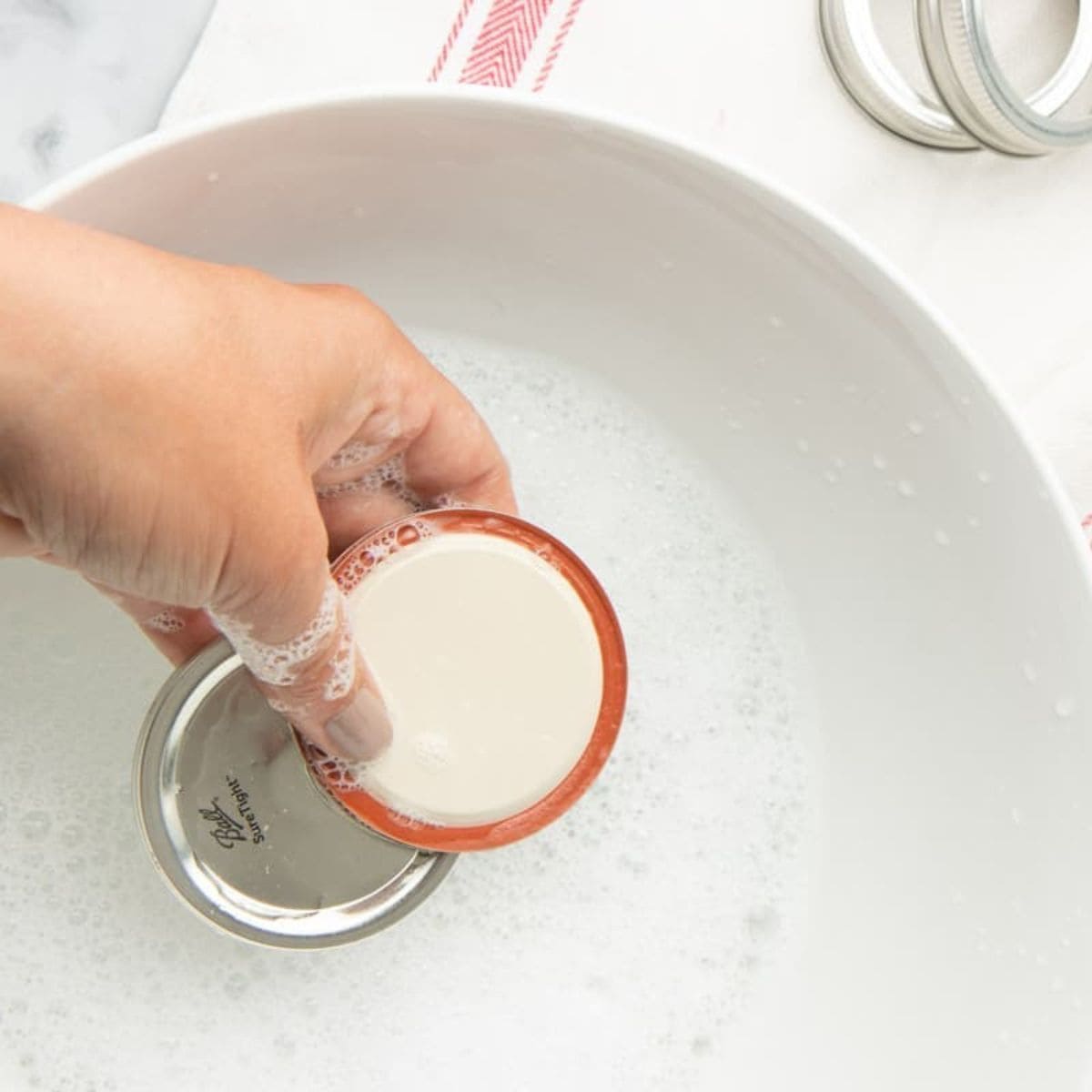 Hand washing canning lids in a bowl of soapy water