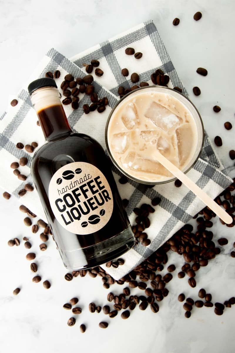 Overhead of a bottle of handmade coffee liqueur lying next to a mixed white russian cocktail.