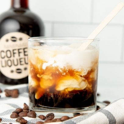 A wooden stirrer mixes a tumbler filled with homemade kahlua, vodka, and cream into a white russian drink.