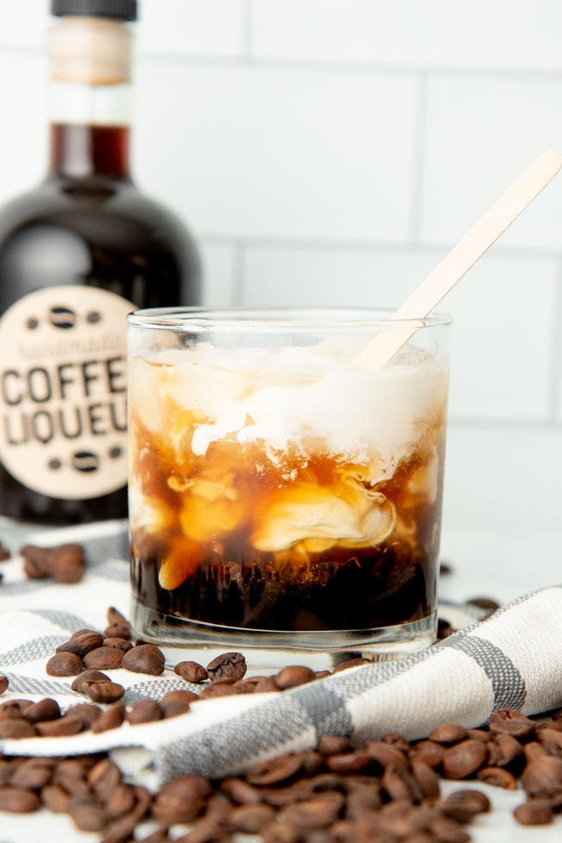 A wooden stirring stick mixes together cream and coffee liqueur into a white russian.