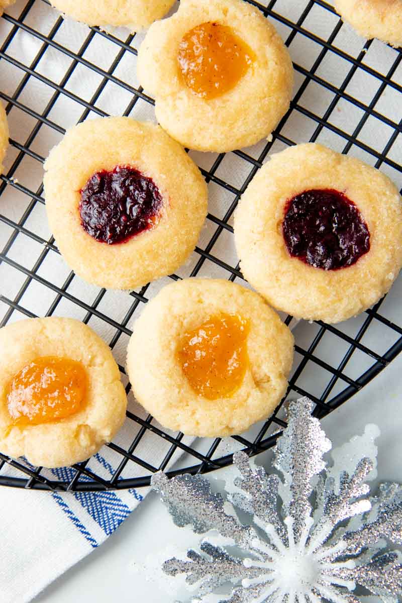 Overhead of baked shortbread cookies filled with jam on a cooling rack.