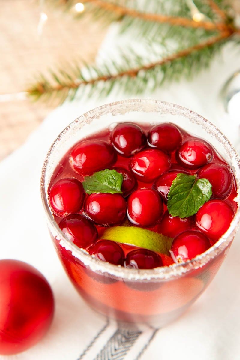Close-up of the top of a glass of punch garnished with cranberries, limes, and mint.