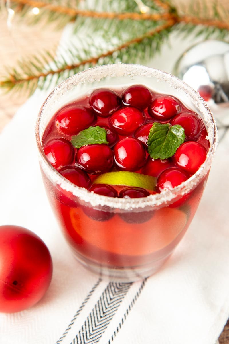 Close-up of a glass of holiday punch surrounded by Christmas ornaments and pine branches.